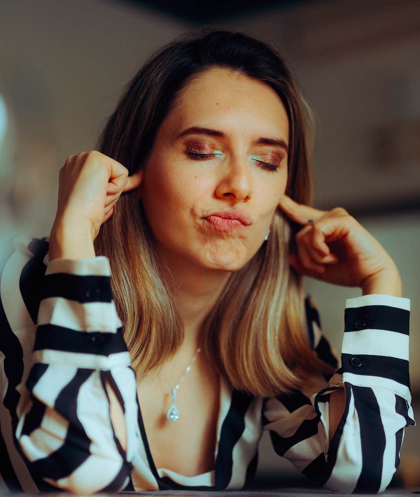 anxious woman eyes closed, fingers in ears